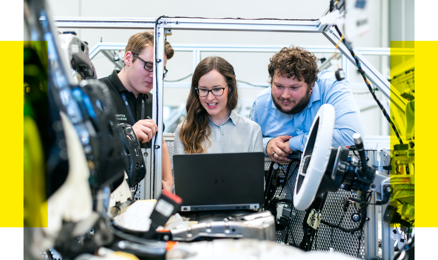 Drei Personen programmieren am Laptop die Technik eines Kraftfahrzeugs