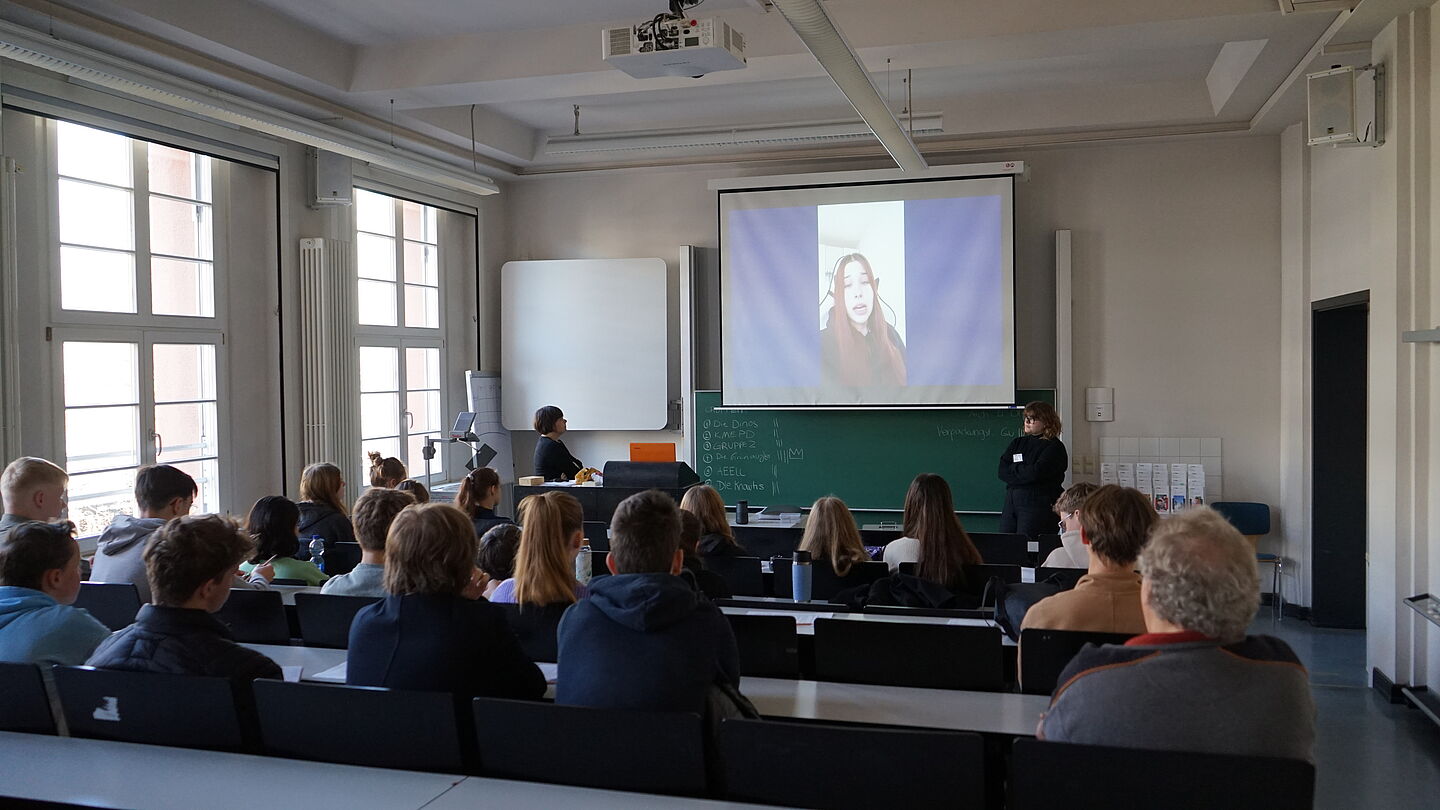 Die Schulklassen schaut sich das Video auf einer Leinwand im Seminarraum an.