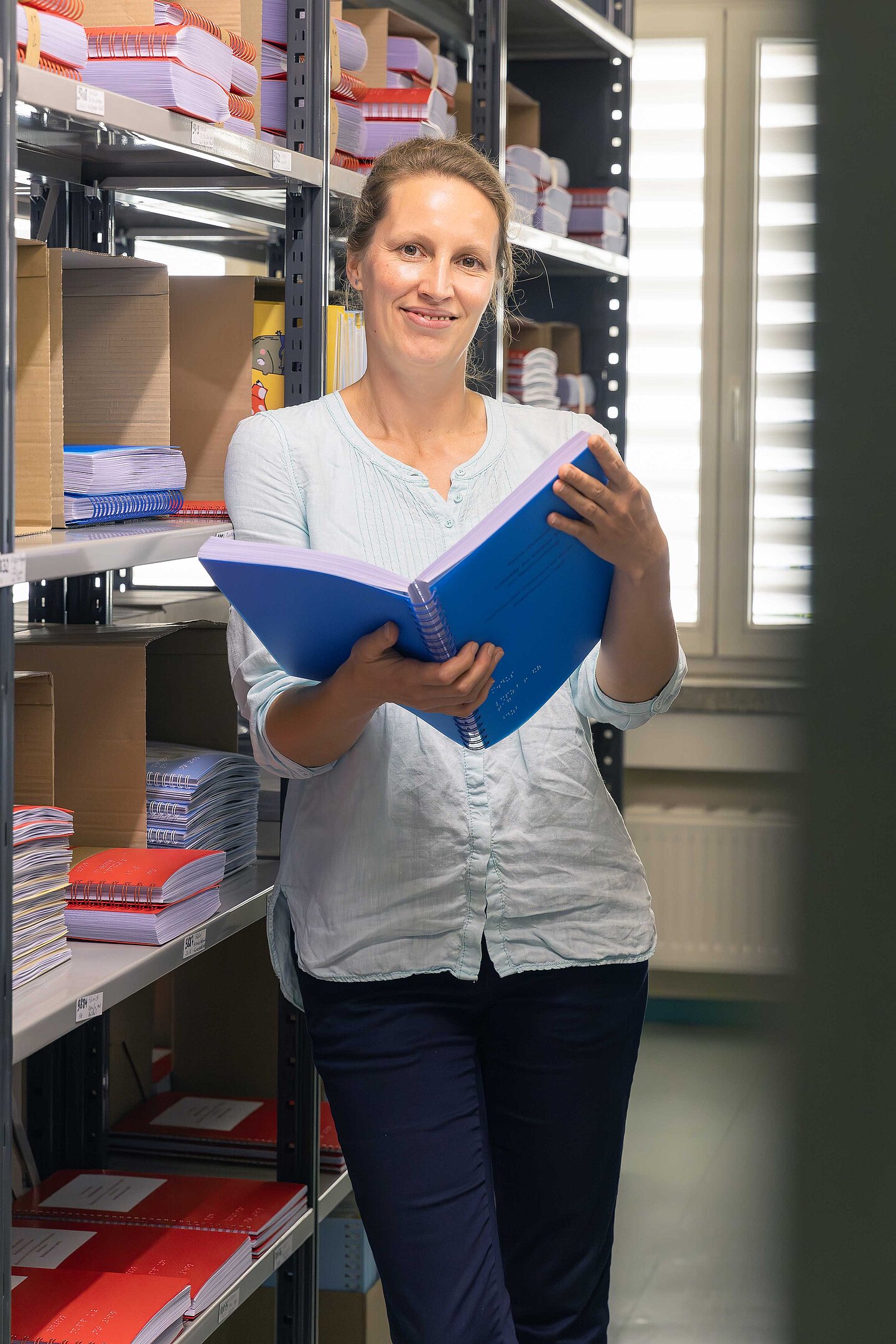 Dr. Julia Dobroschke eine Frau steht in der Bibliothek und hält ein geöffnetes Buch in der Hand