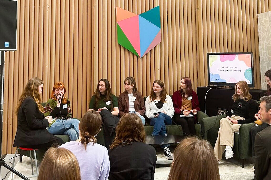 Mehrere Studierende sitzen bei einer Podiumsdiskussion vor interessiertem Publikum.