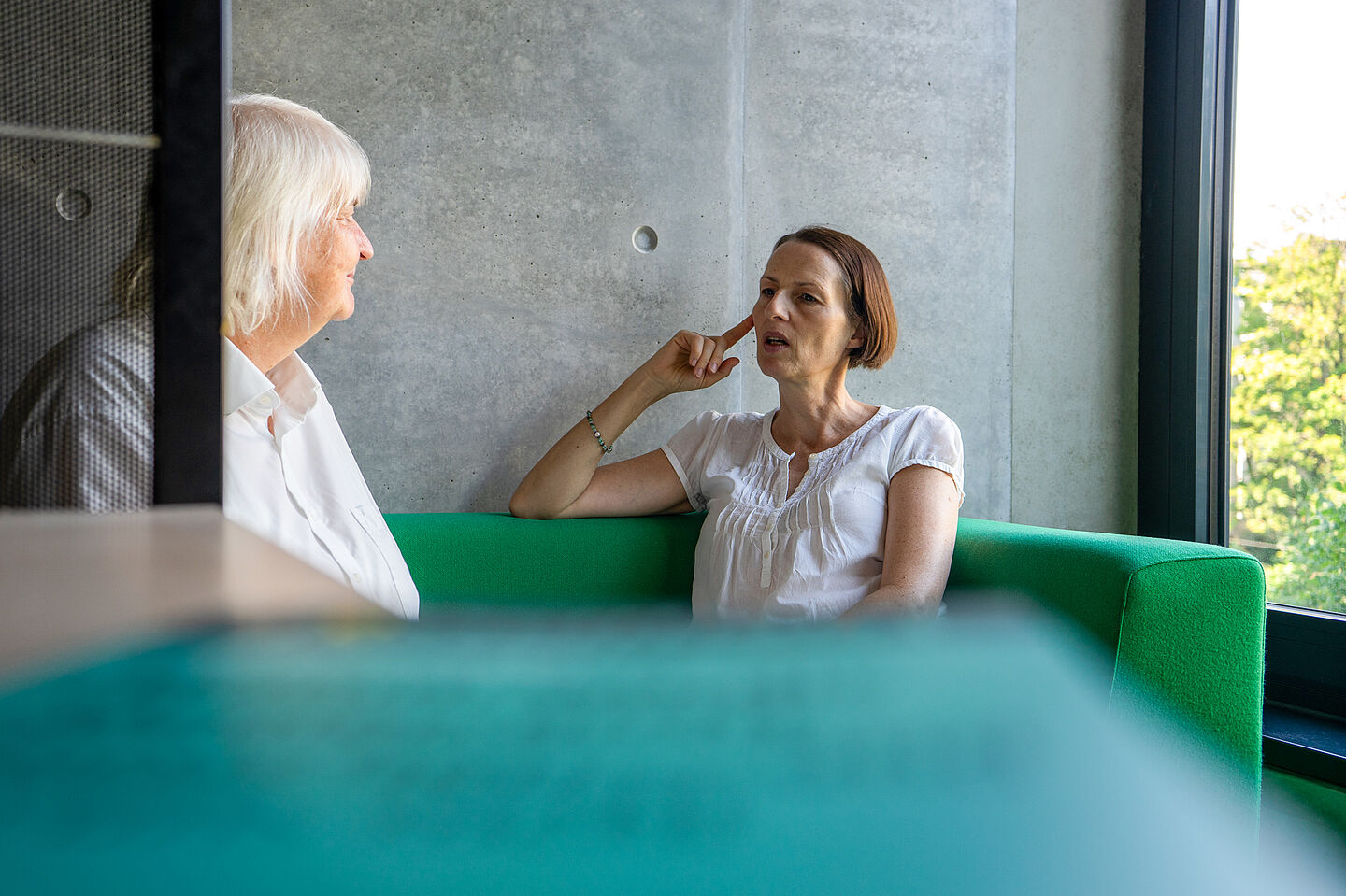 Beide Damen sitzen entspannt auf einer Couch in der Hochschulbibliothek