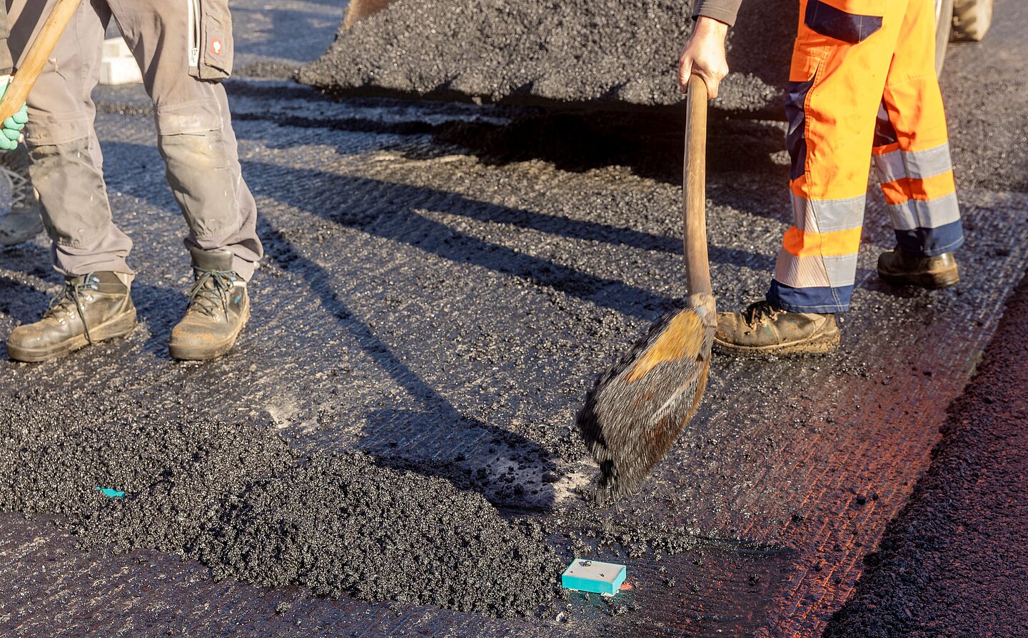 Arbeiter schütten heißen Asphalt auf die Sensoren