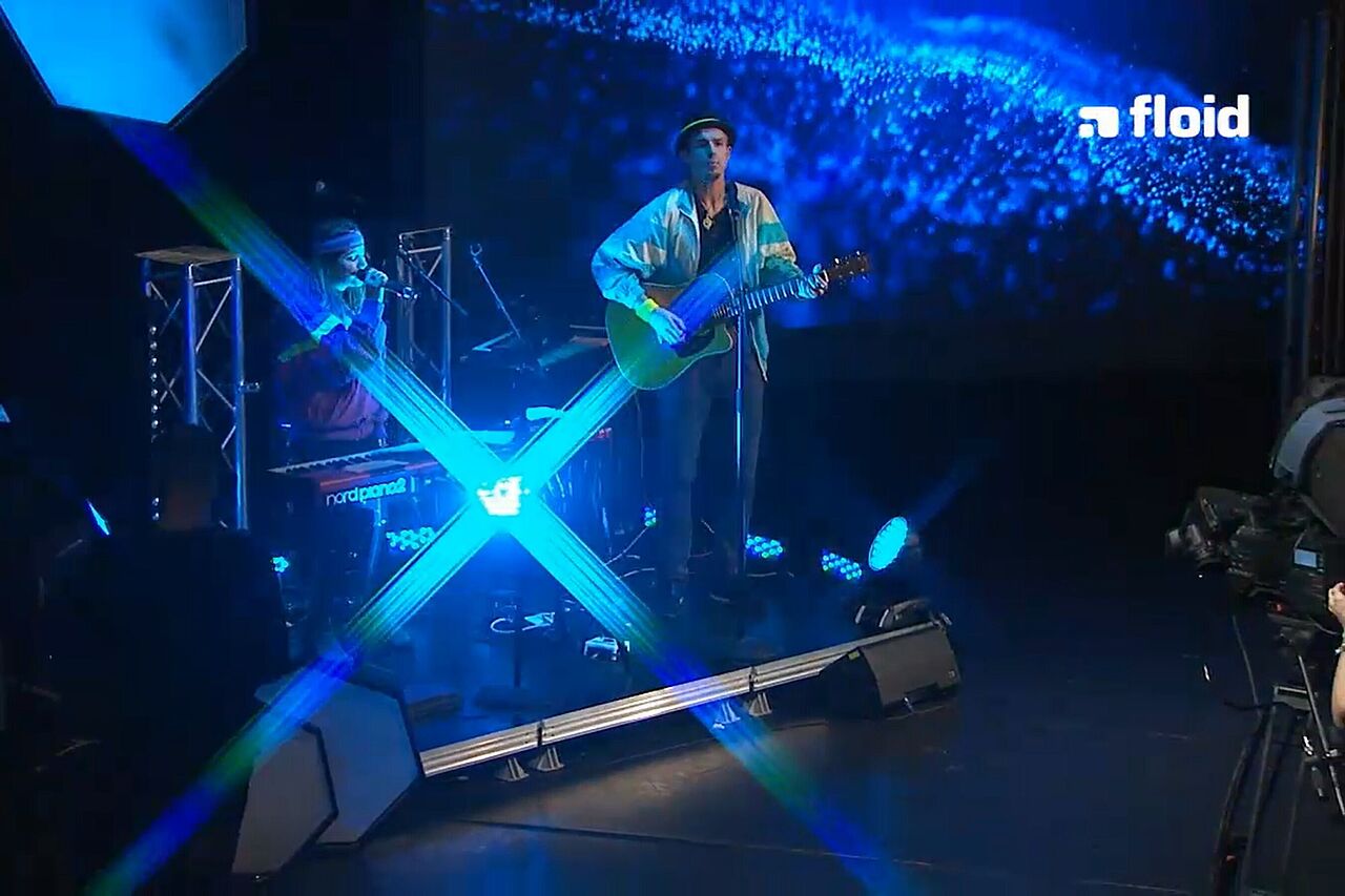 Zwei Personen mit Gitarre und Mikro auf der Bühne, umrahmt von Dunkelheit, die mit blauen Licht-Highlights für Stimmung sorgt