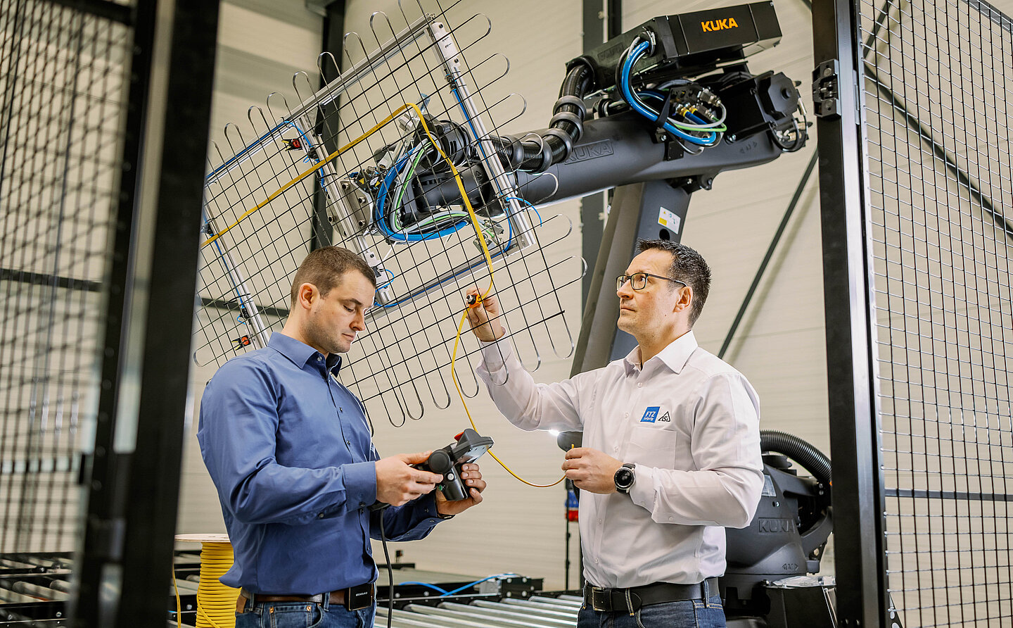 zwei Männer stehen in einer fertigungshalle vor einem Roboterarm