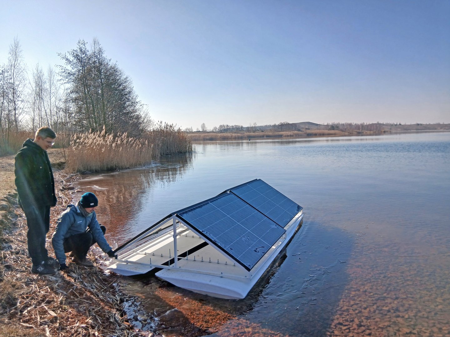 Zwei Männer stehen am See, daneben ein im Wasser schwimmendes Objekt mit PV-Anlage