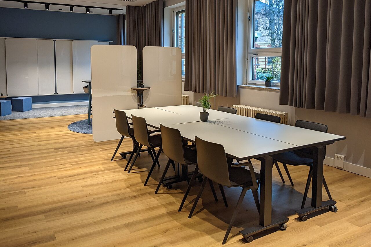 Ein geräumer Raum mit Holzboden und einem Konferenzbereich, bestehend aus einem großen Tisch mit acht Stühlen.