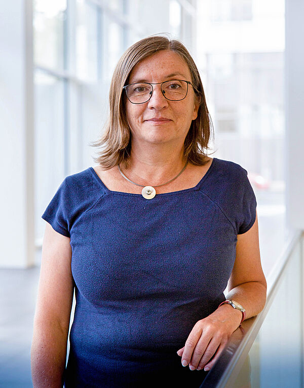 Ein Portraitfoto einer stehenden Frau mit blauem Oberteil