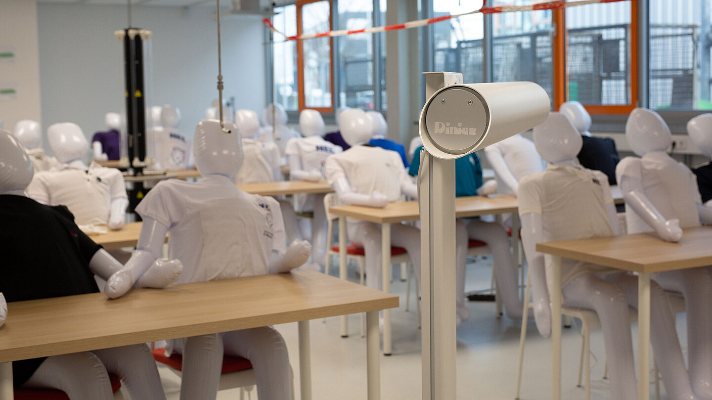 In einem Klassenraum sitzen aufblasbare Puppen mit T-Shirts an Tischen
