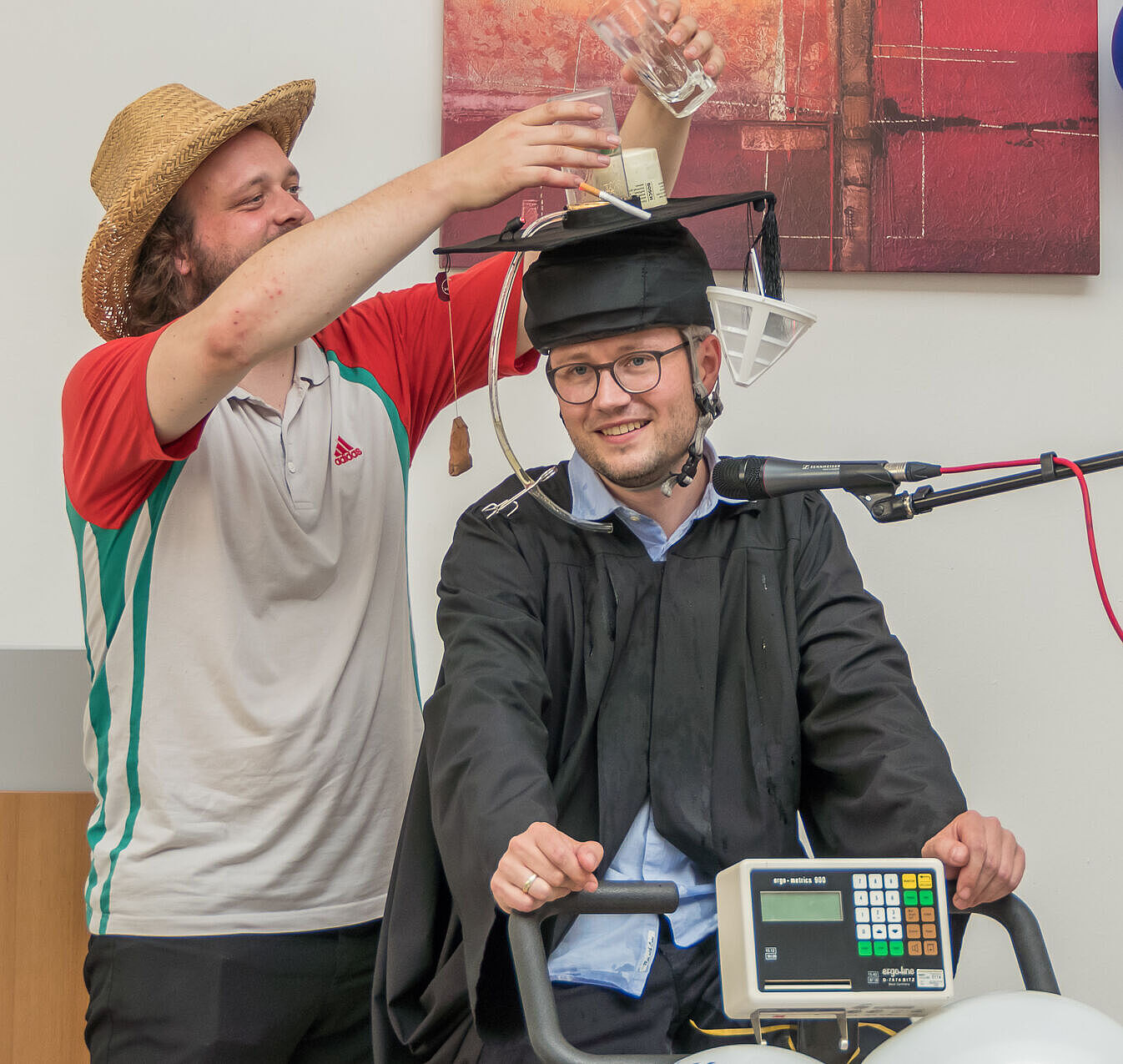 Dr. Andreas Reinhold sitzt auf dem Ergometer. Ein Kollege schüttet eine alkoholische Substanz in ein Gefäß auf seinem Hut.