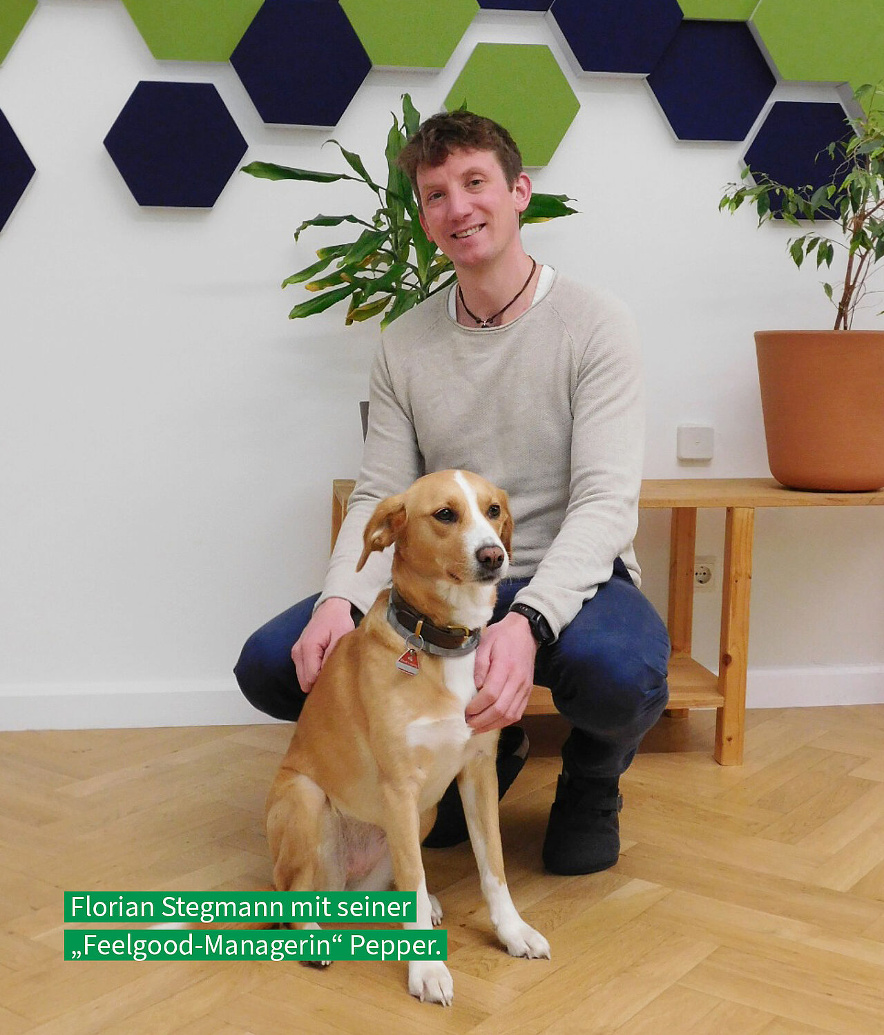 lorian Stegmann kniet lächelnd neben seinem Hund Pepper in einem Büro. Darunter steht der Text: 'Florian Stegmann mit seiner „Feelgood-Managerin“ Pepper.'