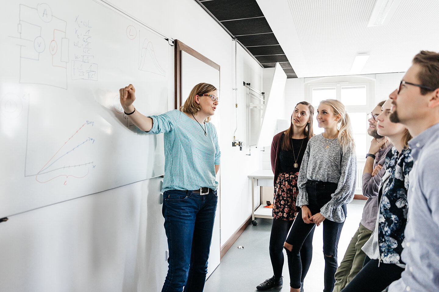 Professorinnen und Professoren gesucht Professorin spricht an der Tafel zu einer Gruppe Studierender