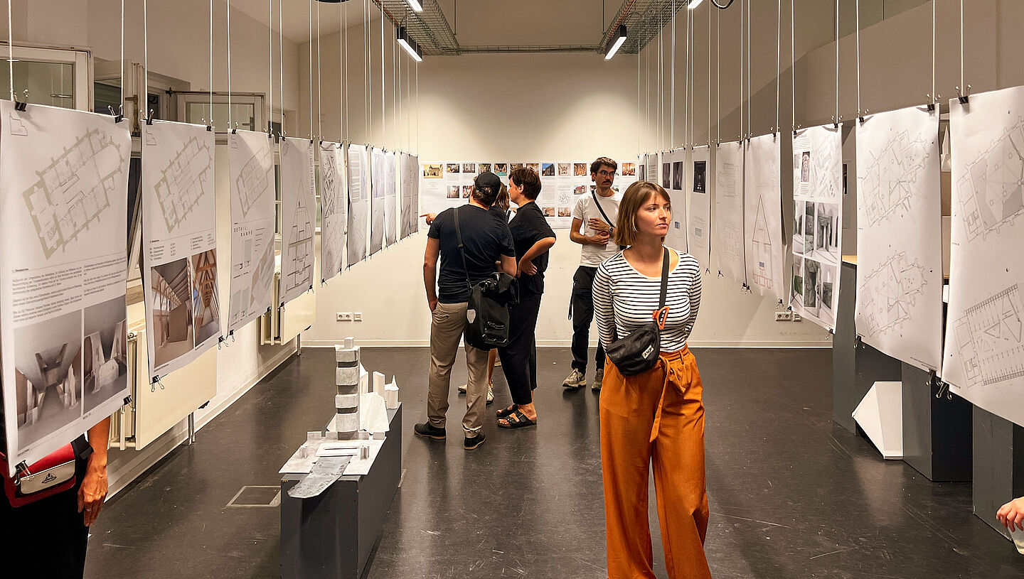 Gäste der Ausstellung laufen entlang von der Decke hängenden Poster