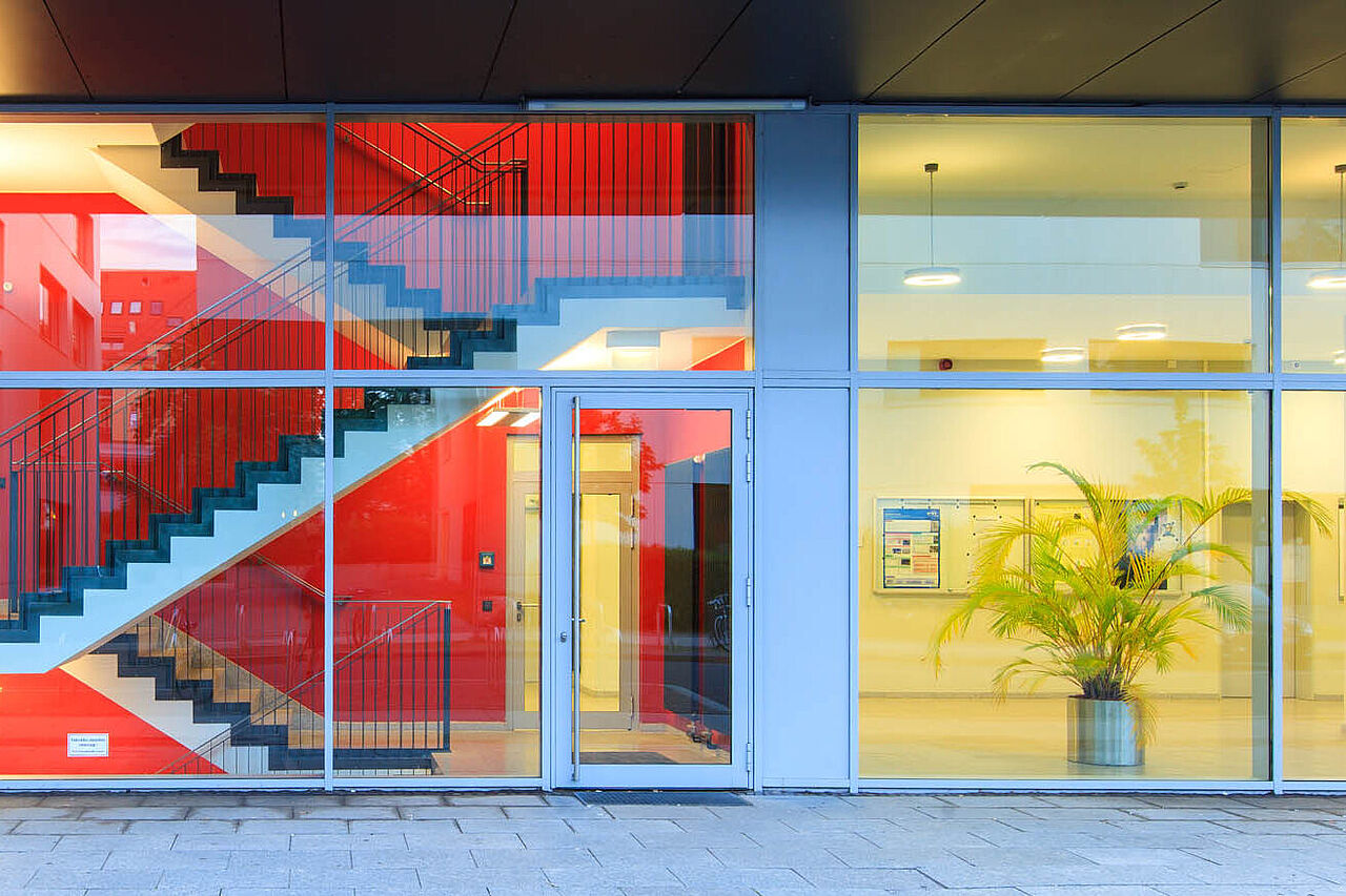 Glasfront eines Hochschulgebäudes mit Blick ins Treppenhaus und in einen Flur.