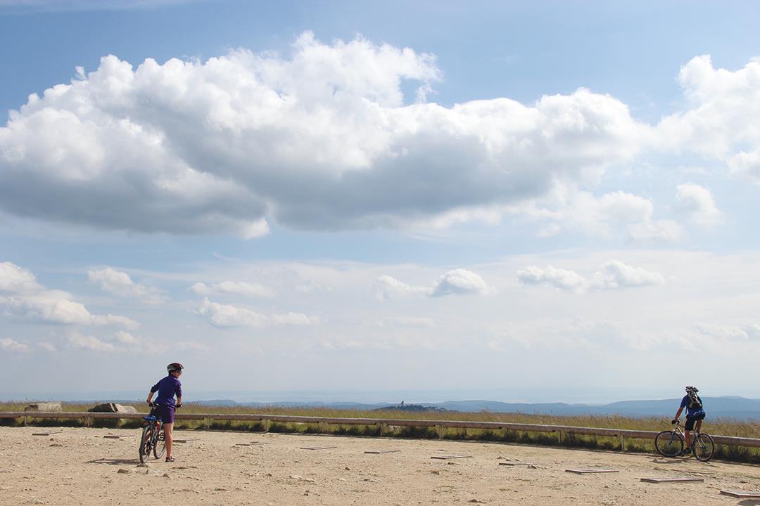 Zwei Radfahrer schauen von einem Plateau auf die umliegende hügelige Landschaft