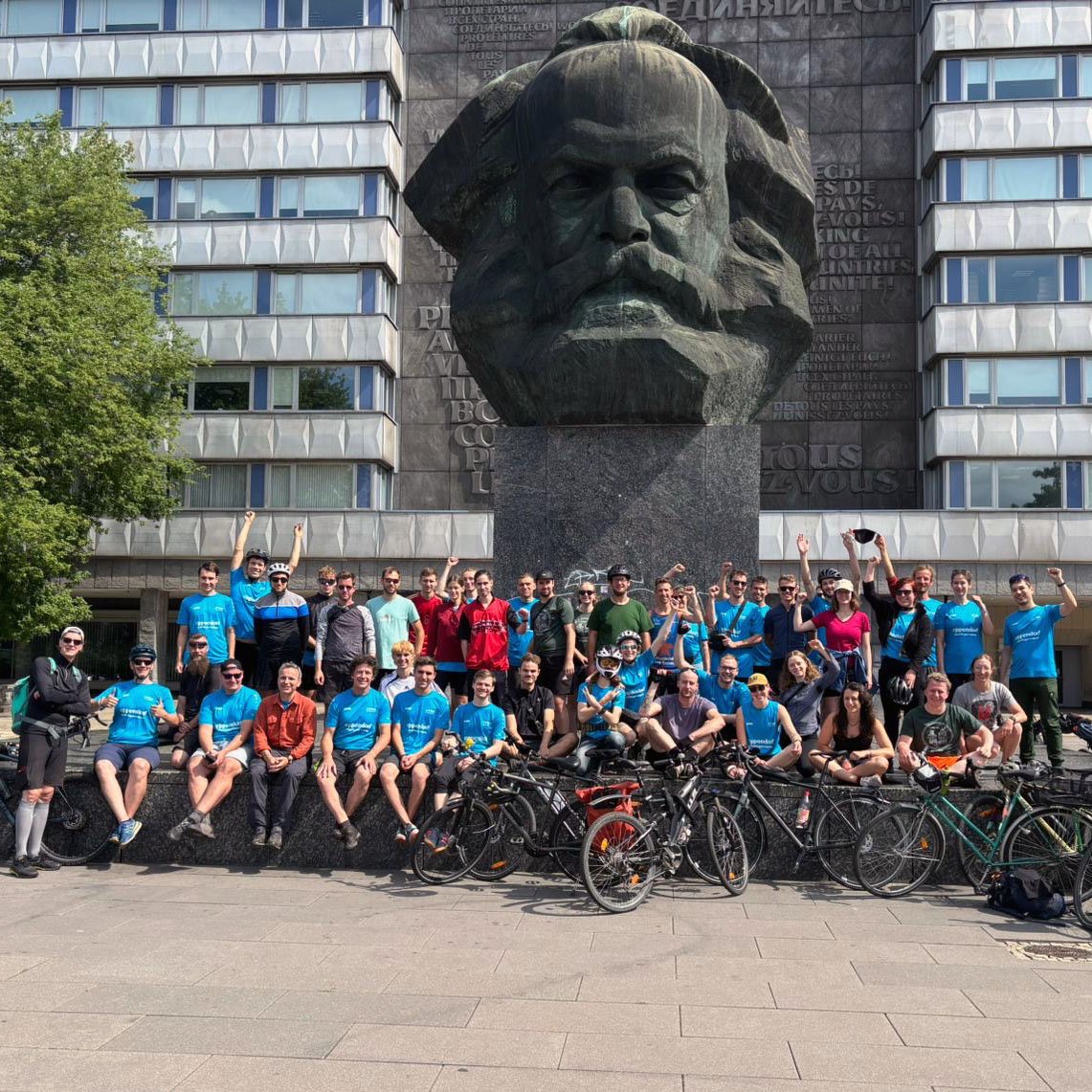 Menschengruppe in Radfahrkleidung mit Fahrrädern vor dem Karl-Marx-Monument in Chemnitz.