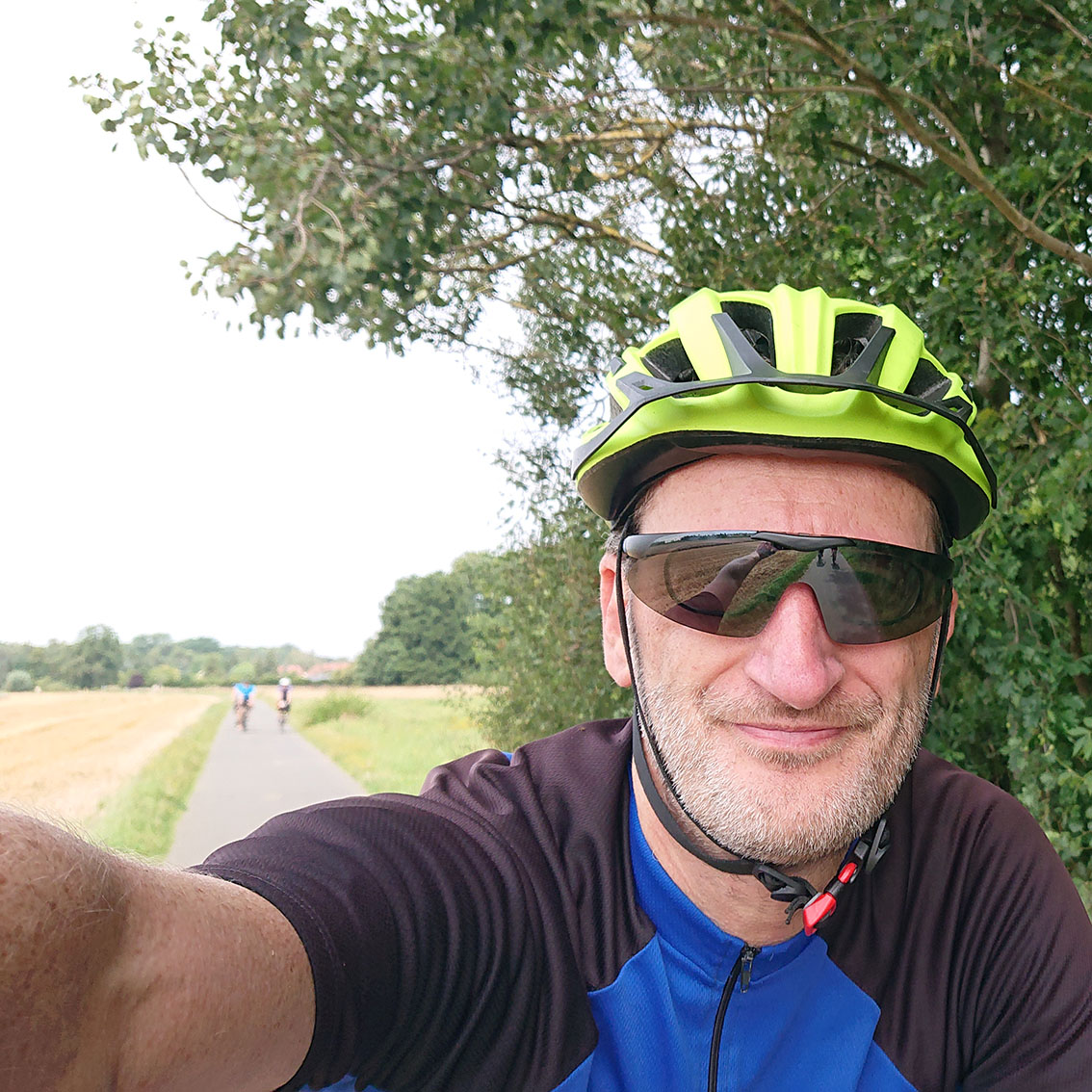 Selfie: Mann mit Fahrradshirt, Helm, Sonnenbrille und Bart beim Radfahren.
