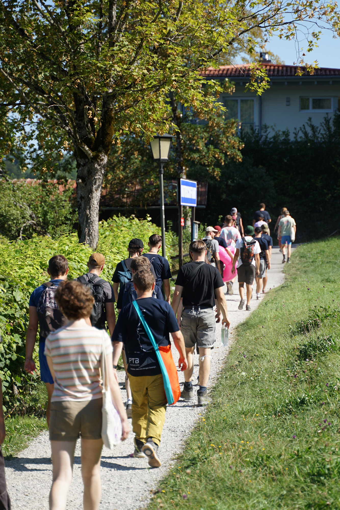 Gruppe von circa 20 Menschen läuft auf einem Pfad entlang einer Hecke und Wiese.